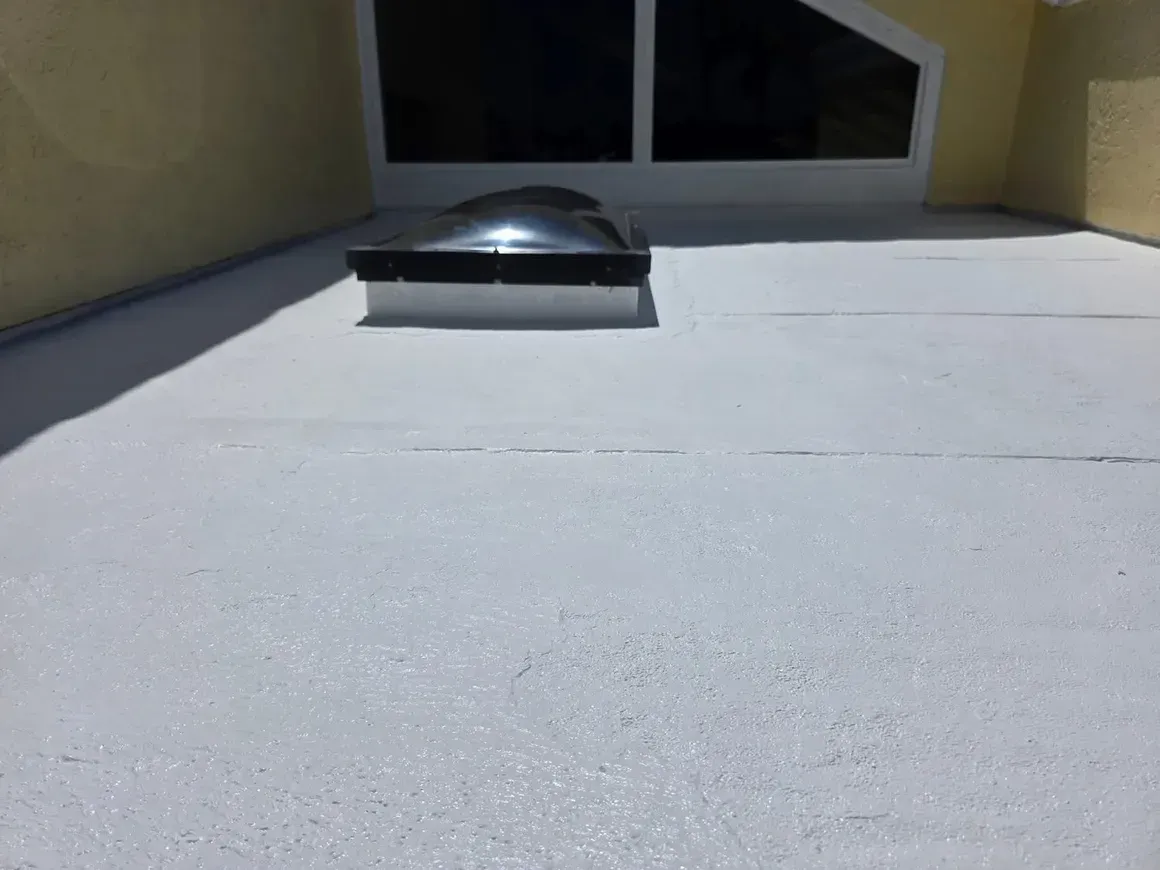 White flat roof with skylight and building in background.