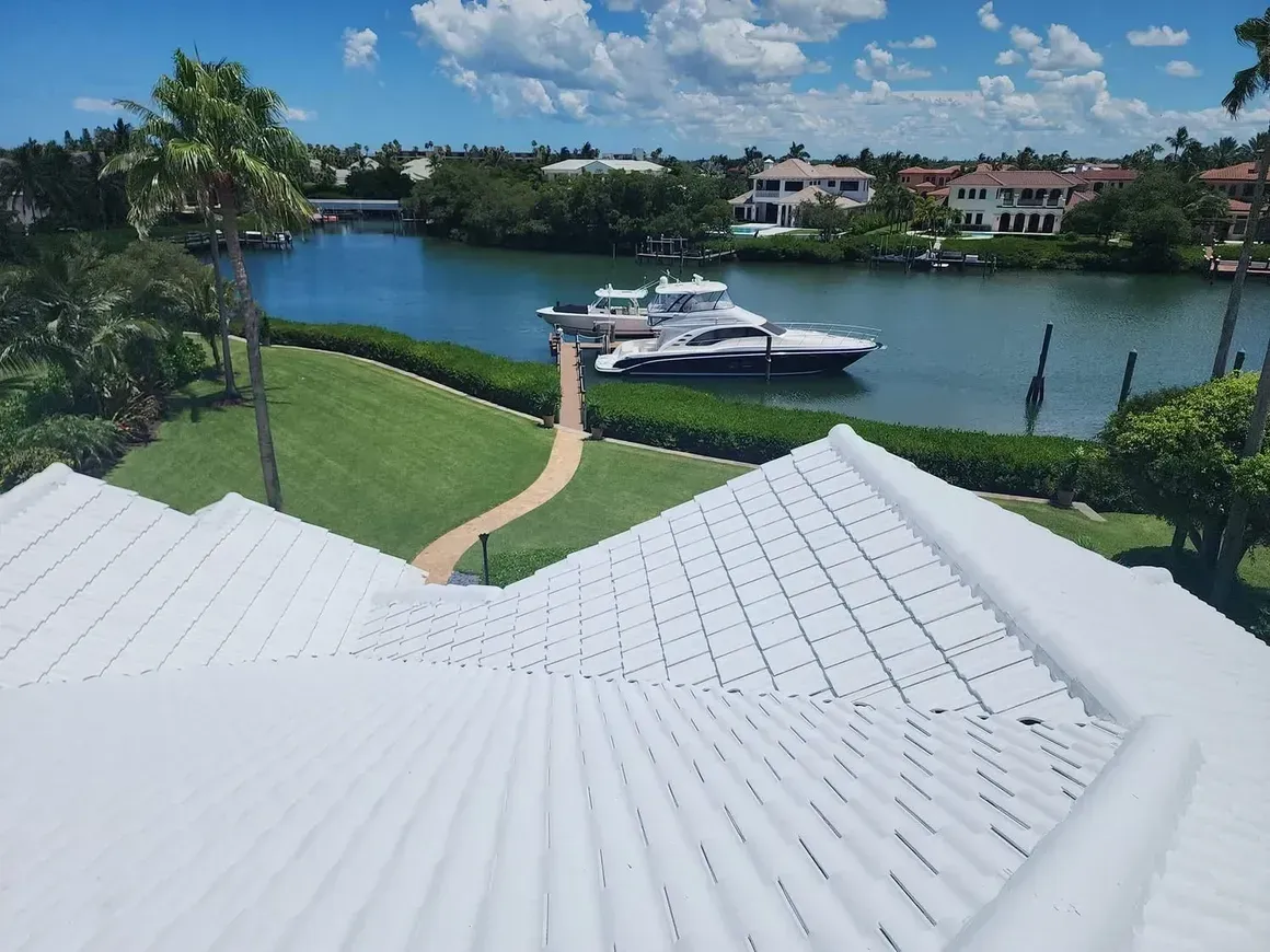 White roof overlooking a waterway with a docked boat, lush green lawn, and houses under a blue sky.