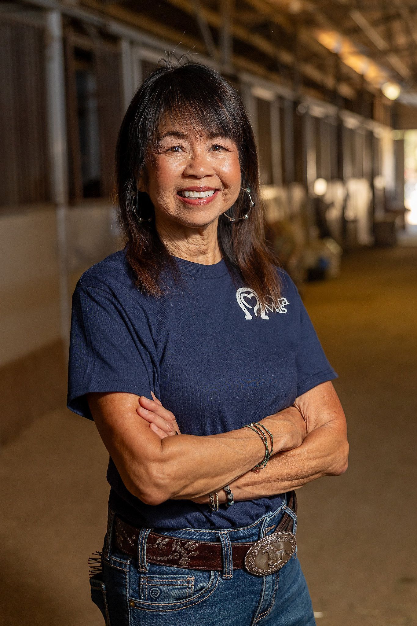 Woman in cowboy hat smiles next to brown horse with heart-shaped marking on forehead, near a fence.