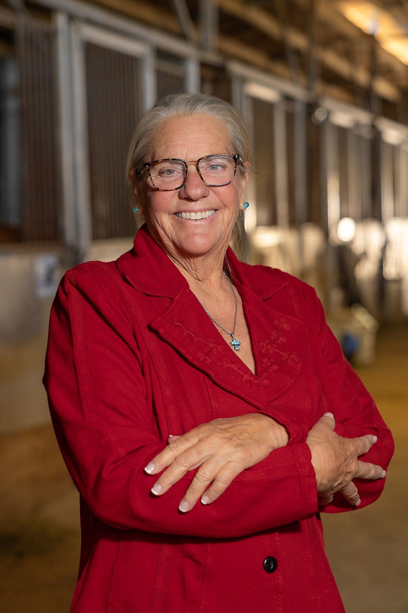 Kathy Holman, Otra Mas Founder Kathy Holman, Otra Mas Founder
Smiling person in a red blazer standing with arms crossed in a warmly lit hallway