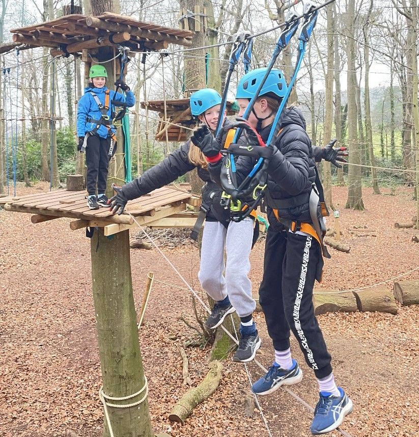 Three people on a treetop adventure course. Two are walking a tightrope, and one is standing on a platform.