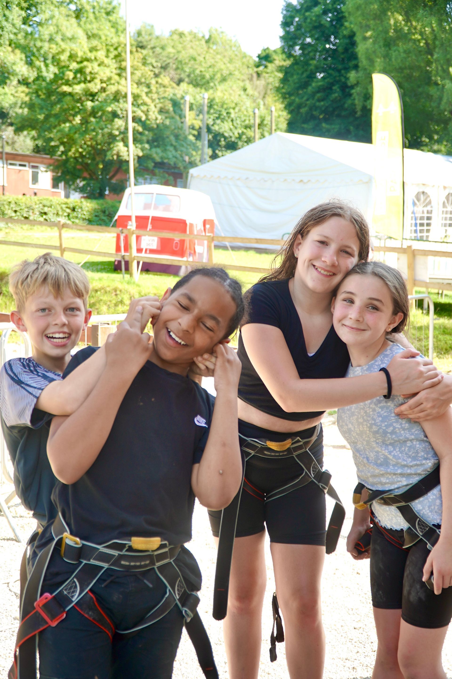Four people wearing harnesses smile at the camera outdoors near a red van and white tent.