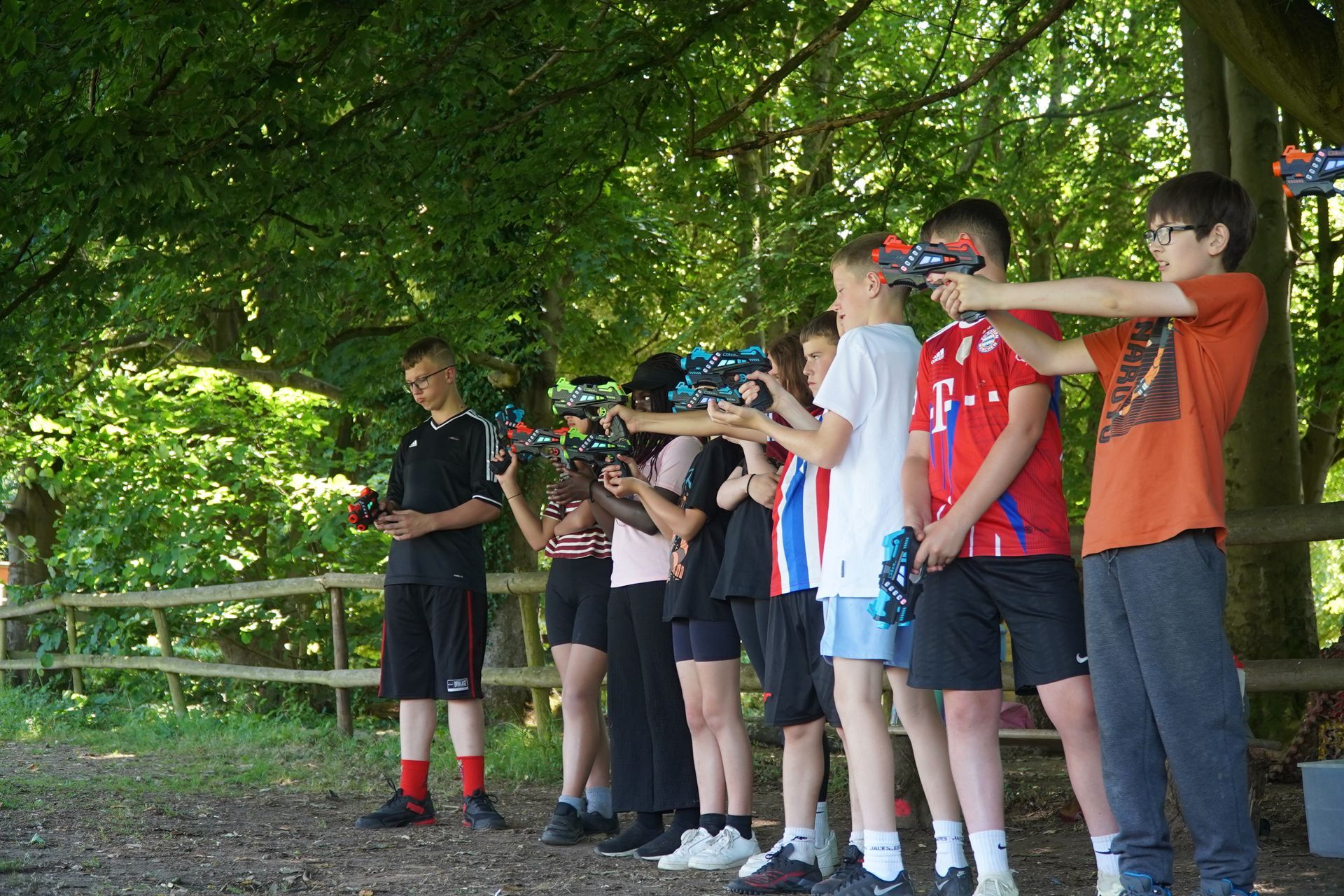Group of kids aiming toy guns outdoors, trees in background.