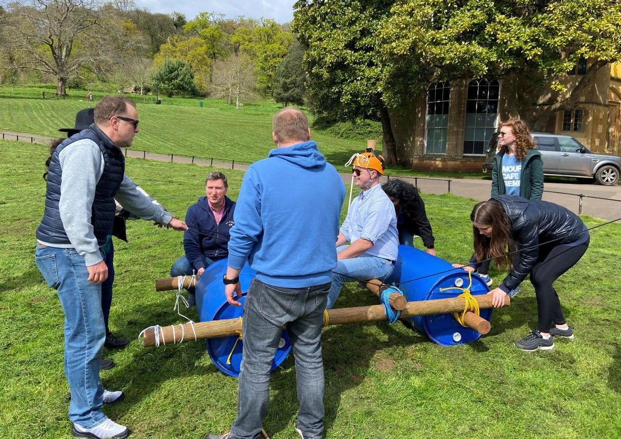 Group of people assembling a raft made of barrels and wood on grass, outdoors. outdoor activities near me