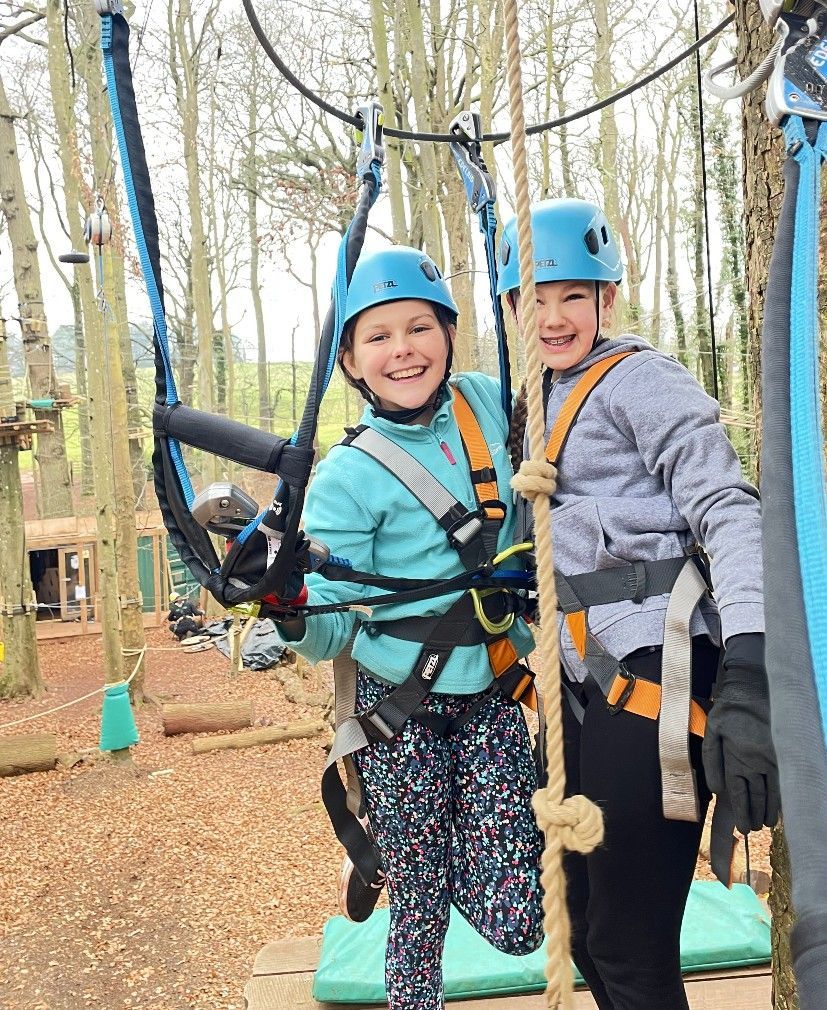 Two children in helmets and harnesses at an adventure park, smiling and ready to zipline. high ropes course 