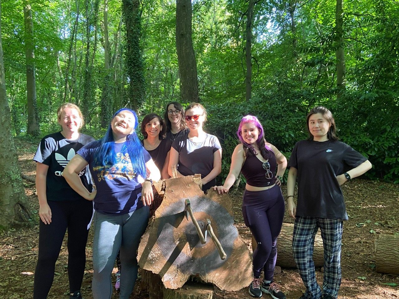 Group of people smiling in a forest, standing behind a wooden stump with a painted lightning bolt.