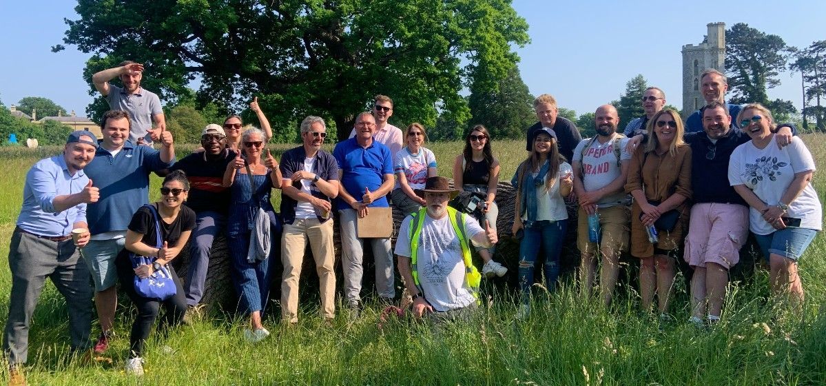 Group of people posing outdoors in a field, with a tree and building in the background. adventure activities