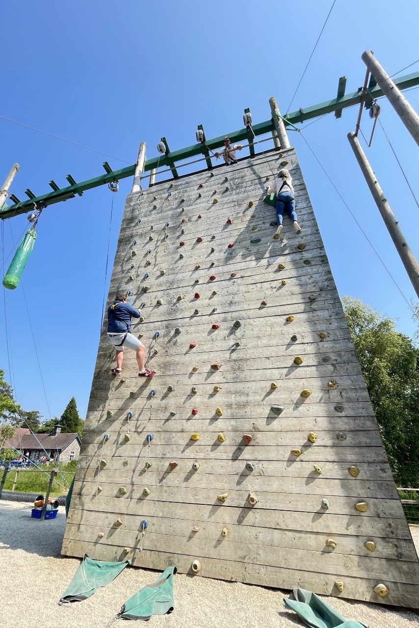 People climb a tall outdoor rock wall. Blue sky.