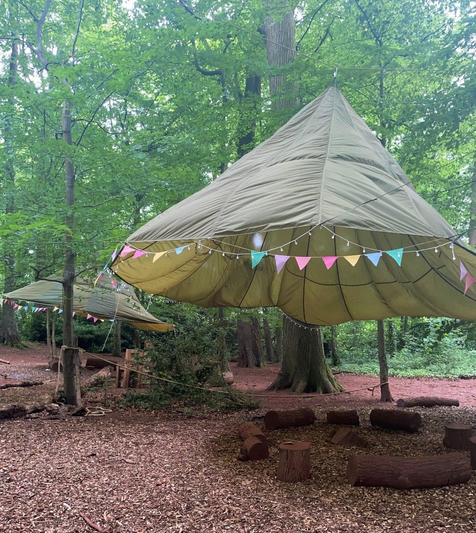 Two outdoor structures in a forest with green canopies decorated with colorful pennants.