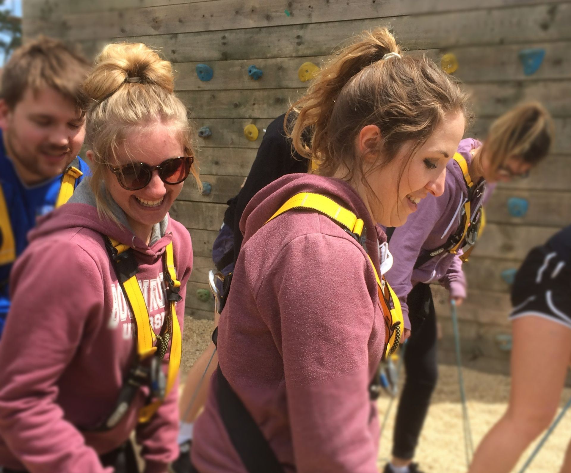 People in climbing harnesses smile near a climbing wall outdoors. adventure activities