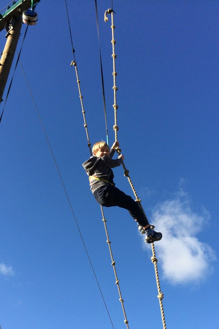 Child climbing a rope ladder against a blue sky.