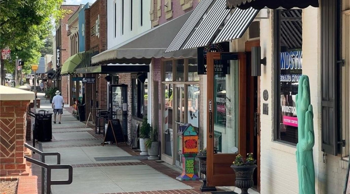 A man is walking down a sidewalk in front of a row of shops.