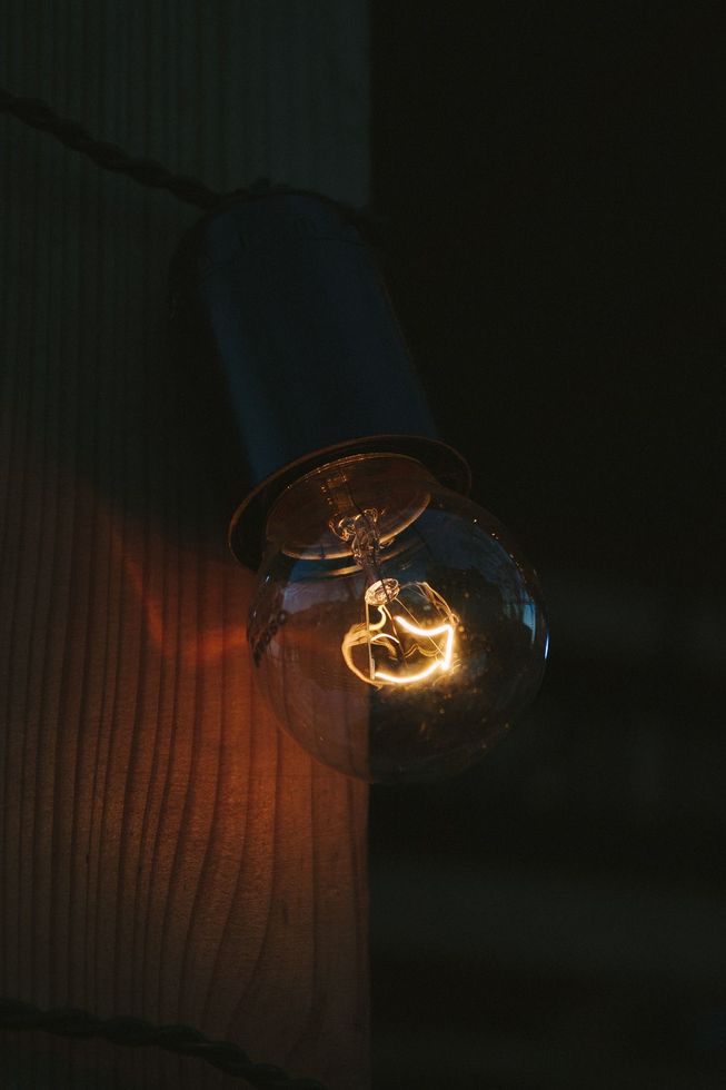Uma única lâmpada brilhante está pendurada em um poste de madeira escura, projetando uma luz suave e quente.