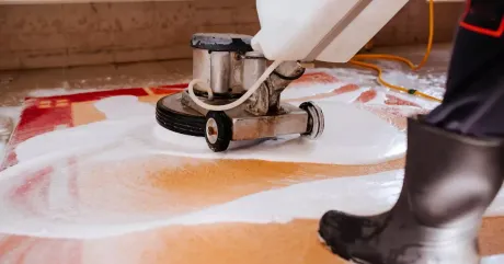 Professional rug cleaning in progress as a floor machine scrubs a colorful area rug with deep-cleaning solution and foam