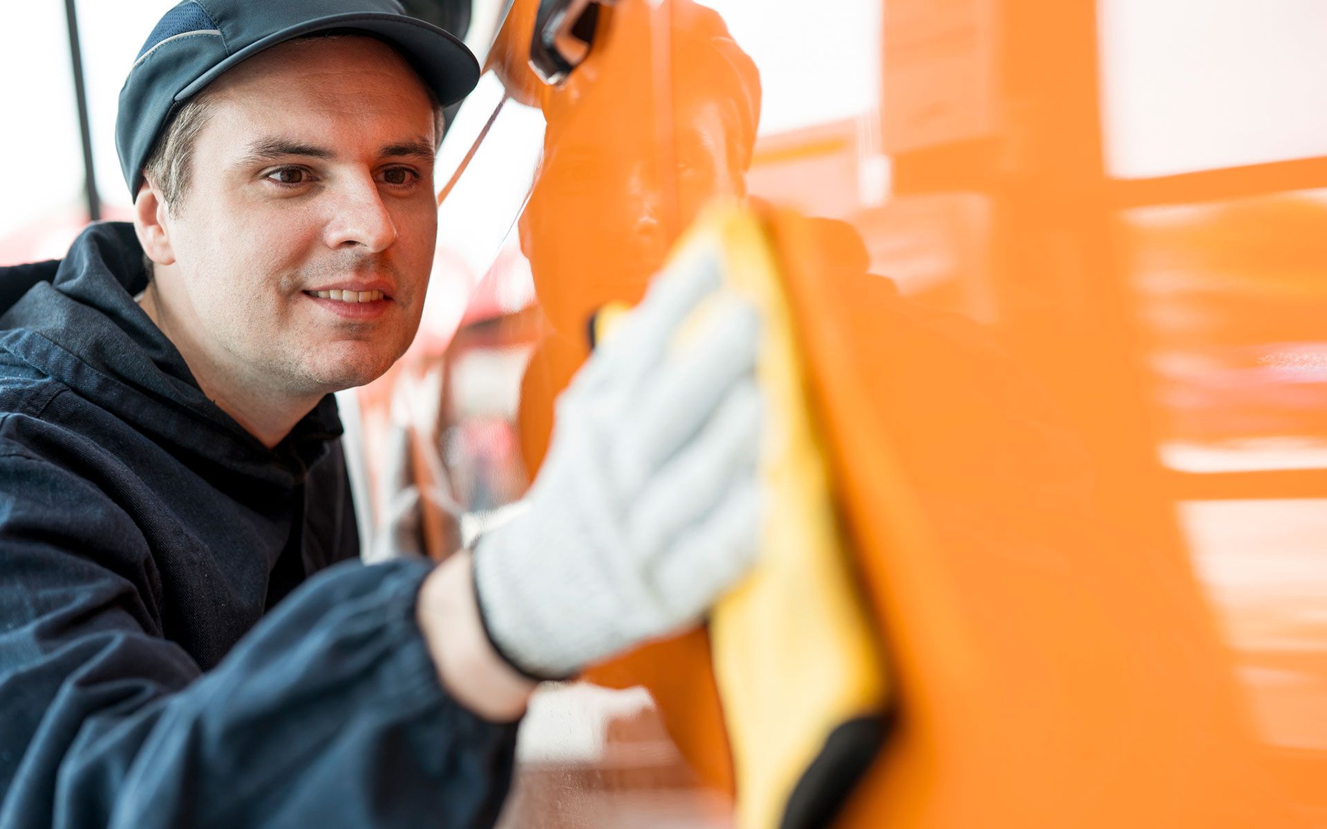 A man is polishing an orange vehicle with a cloth.