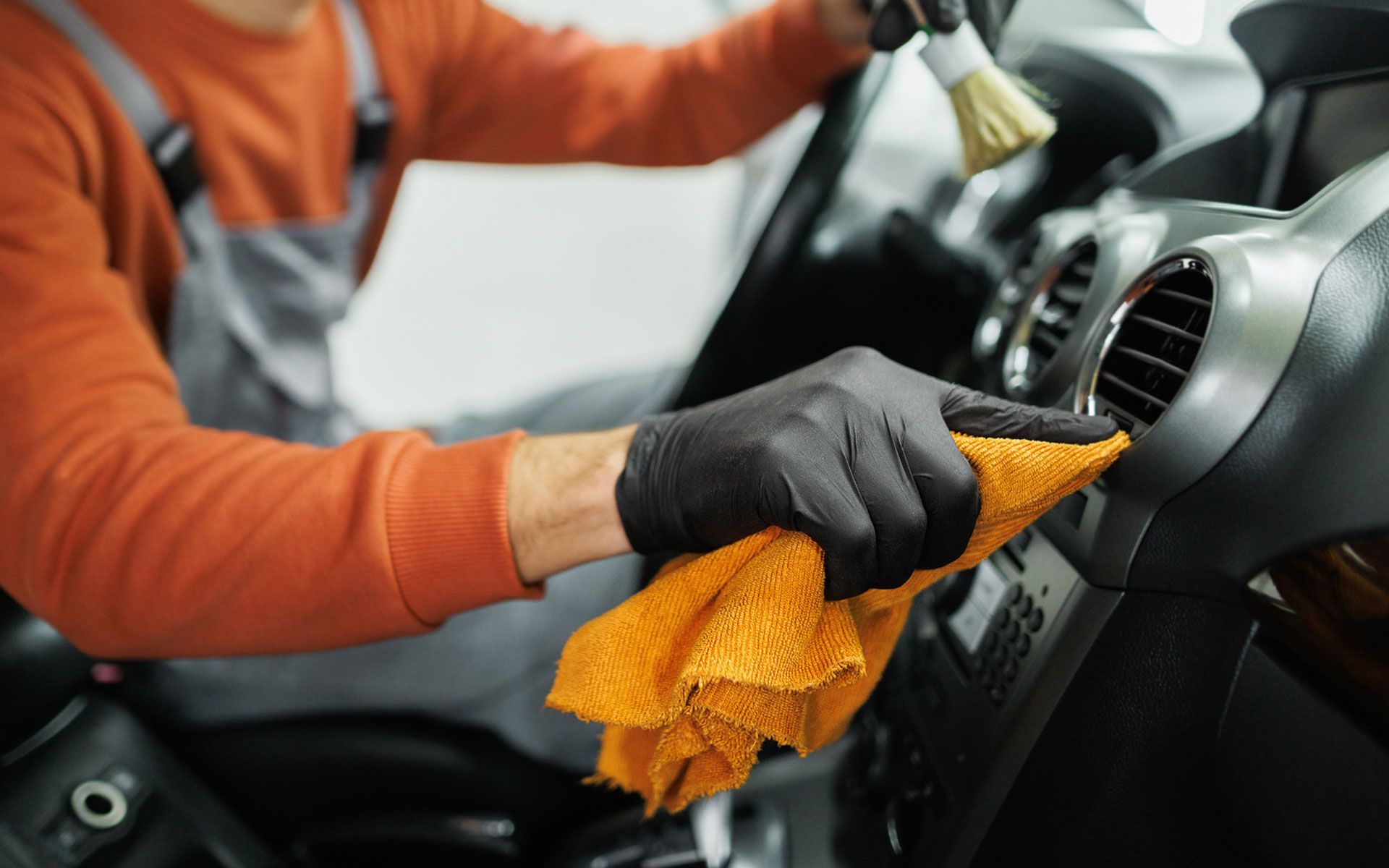 A man is cleaning the dashboard of a car with a towel and brush.