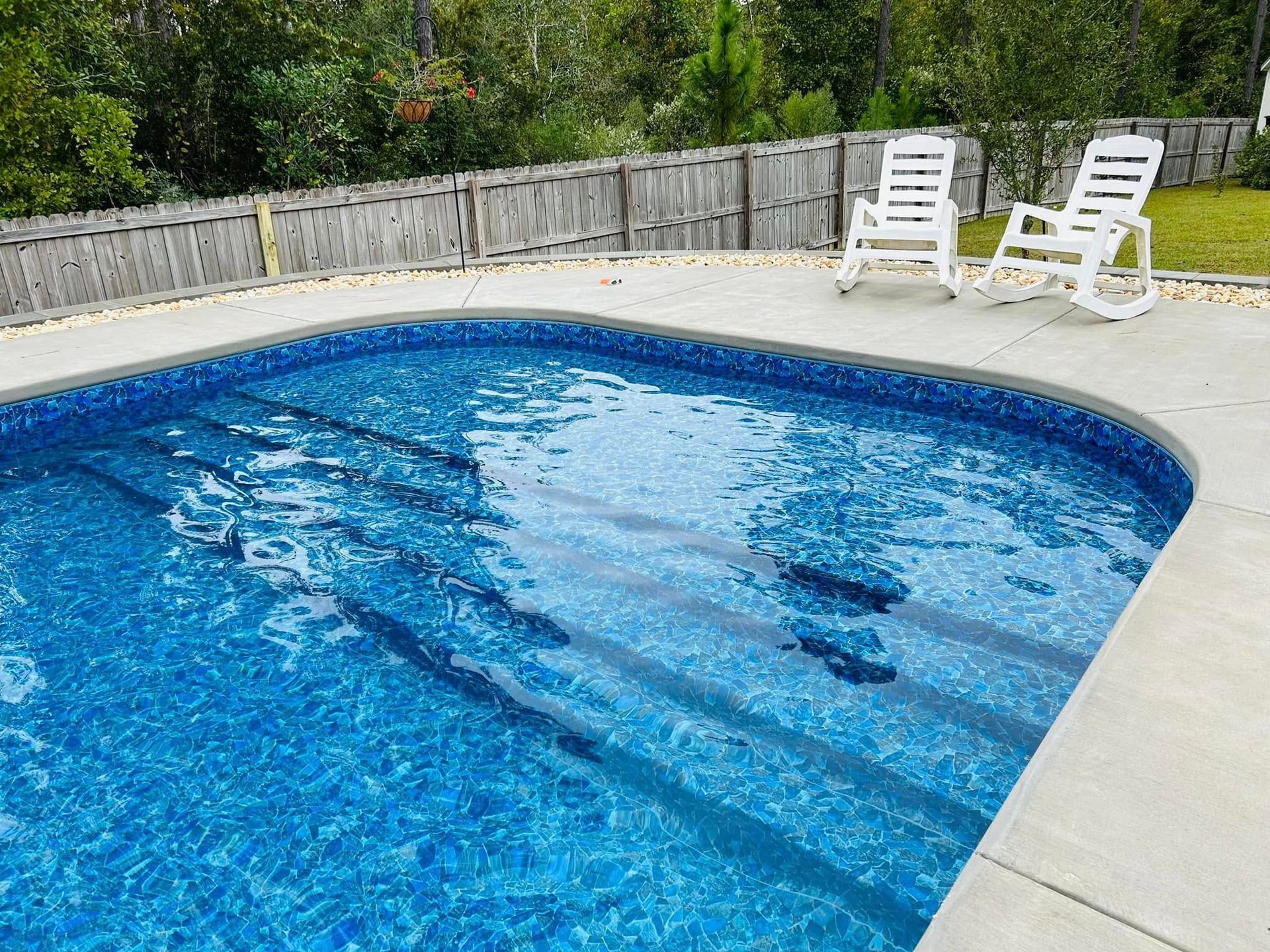 Two white rocking chairs are sitting next to a large swimming pool.