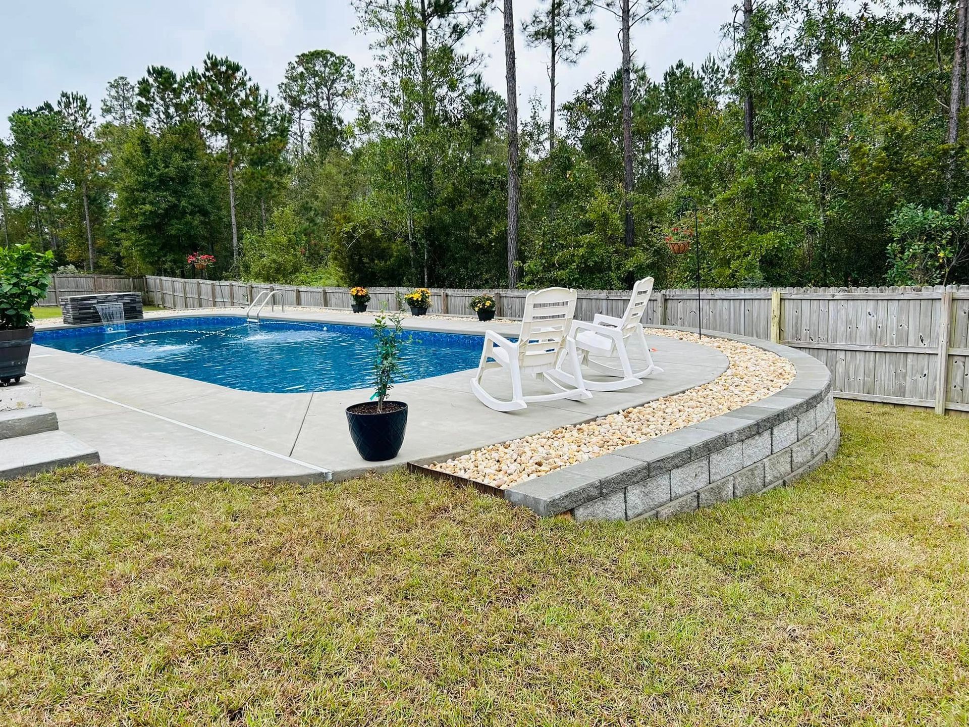 A large swimming pool is surrounded by a fence and rocking chairs.