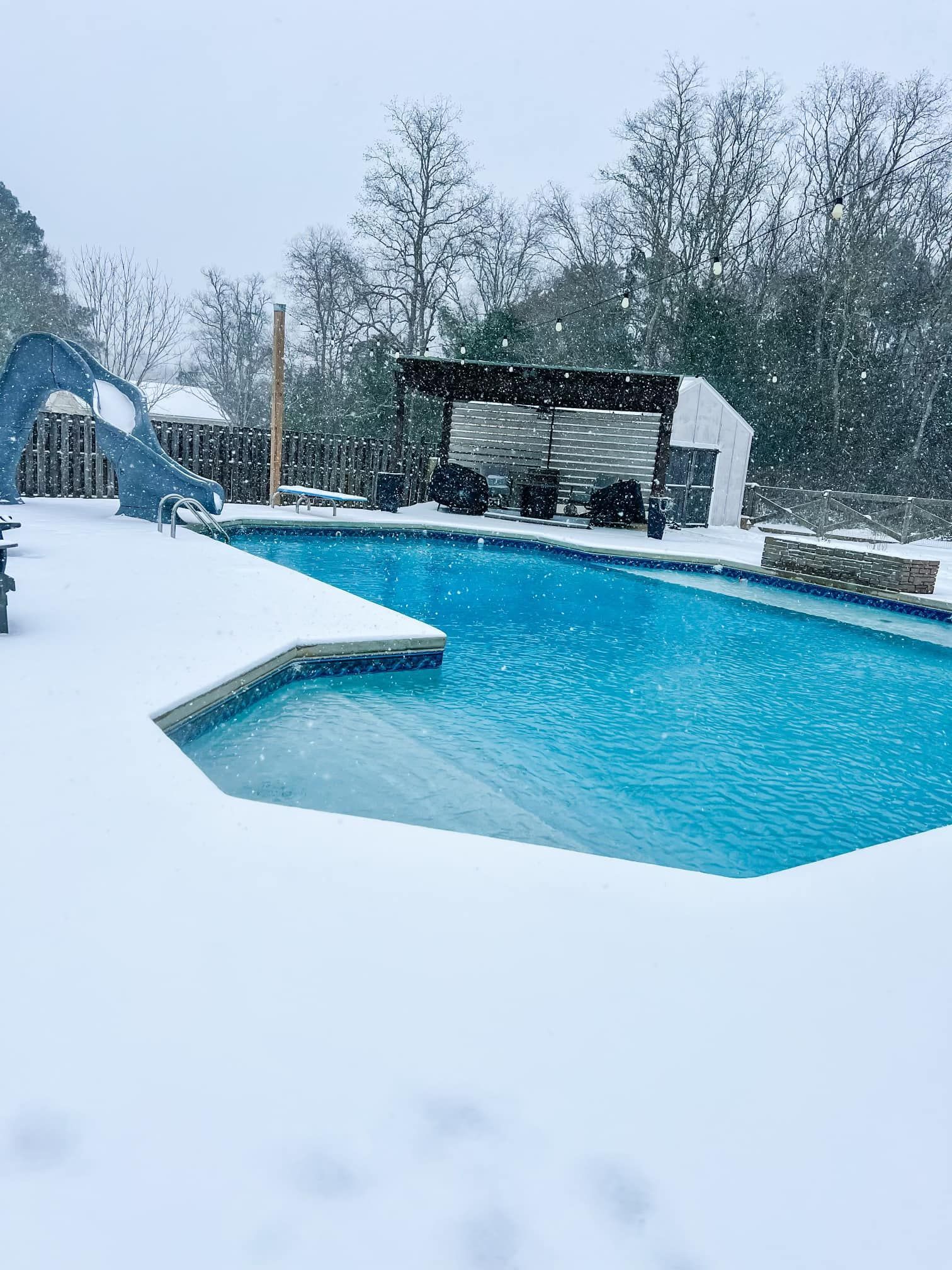 A swimming pool covered in snow with a slide in the background.