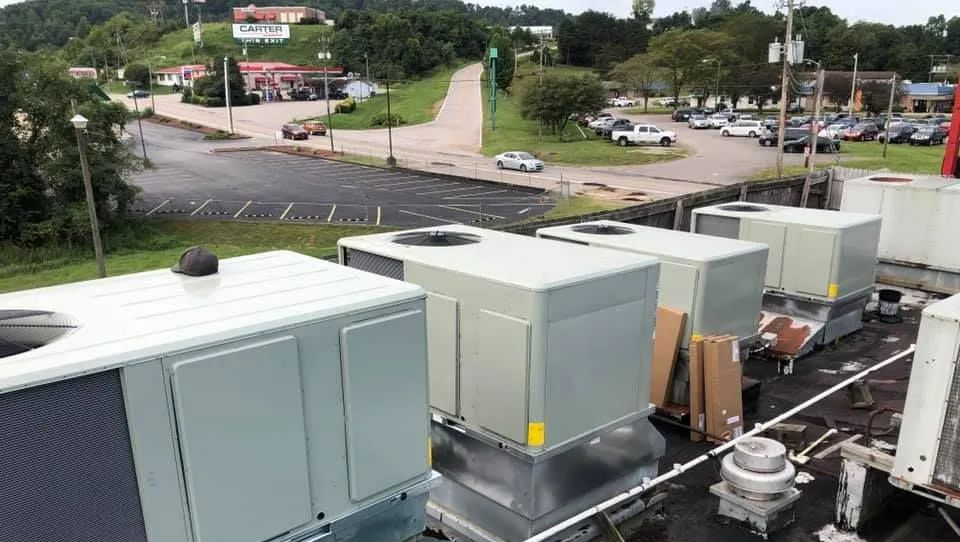 Rooftop HVAC units beside a road and parking lot, with trees and buildings in the background