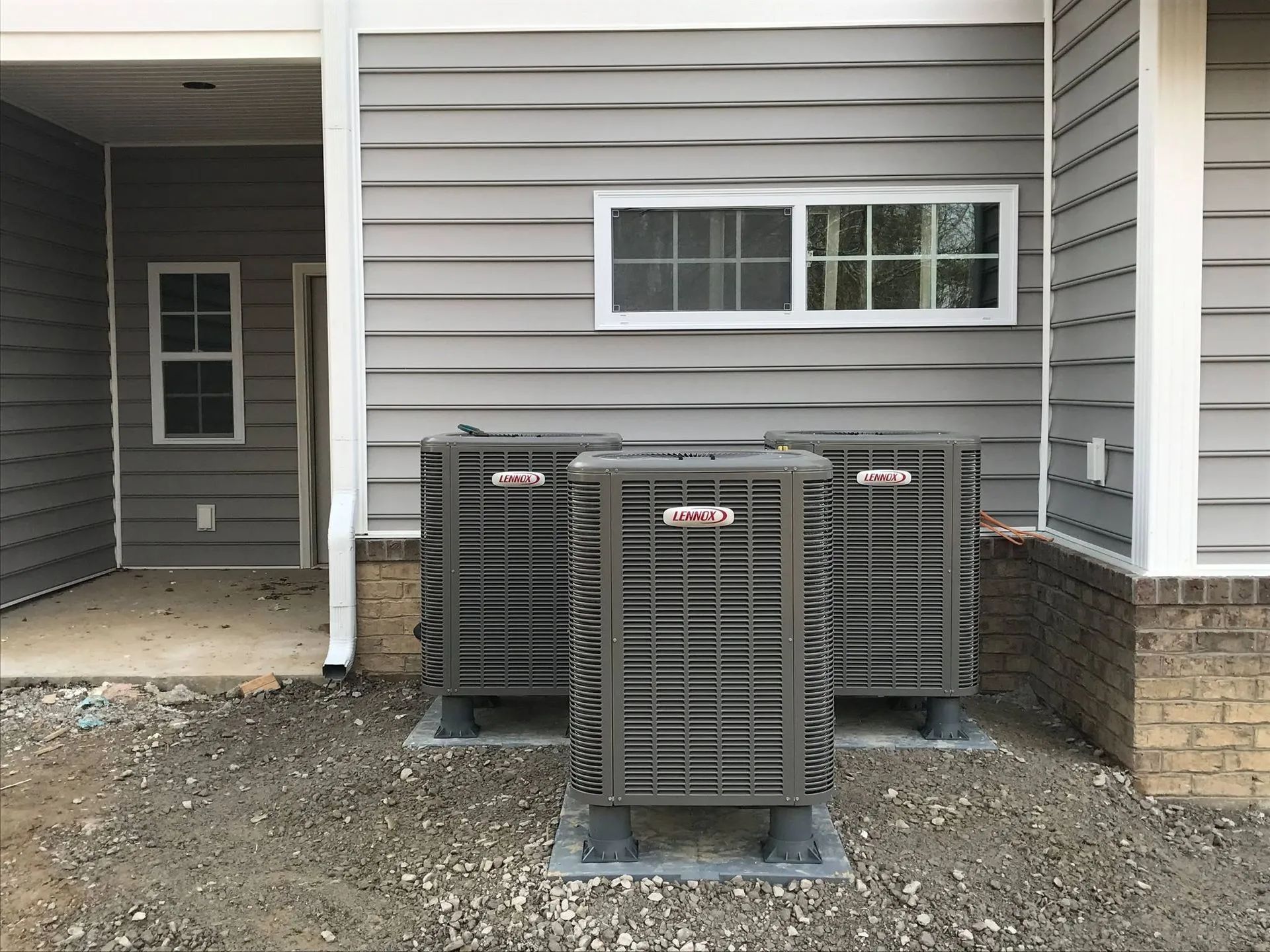 Three gray outdoor HVAC units beside a gray house with a small covered porch.
