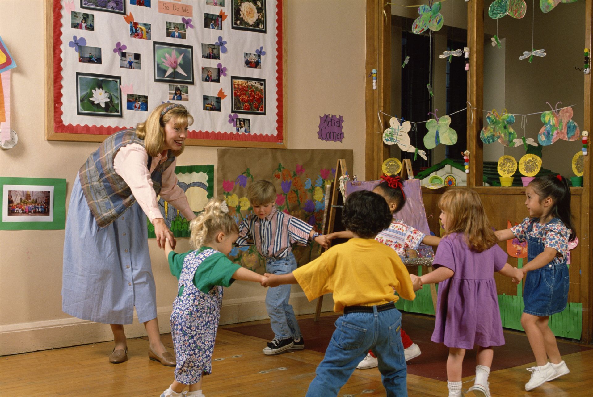 A group of children are holding hands in a circle with their teacher