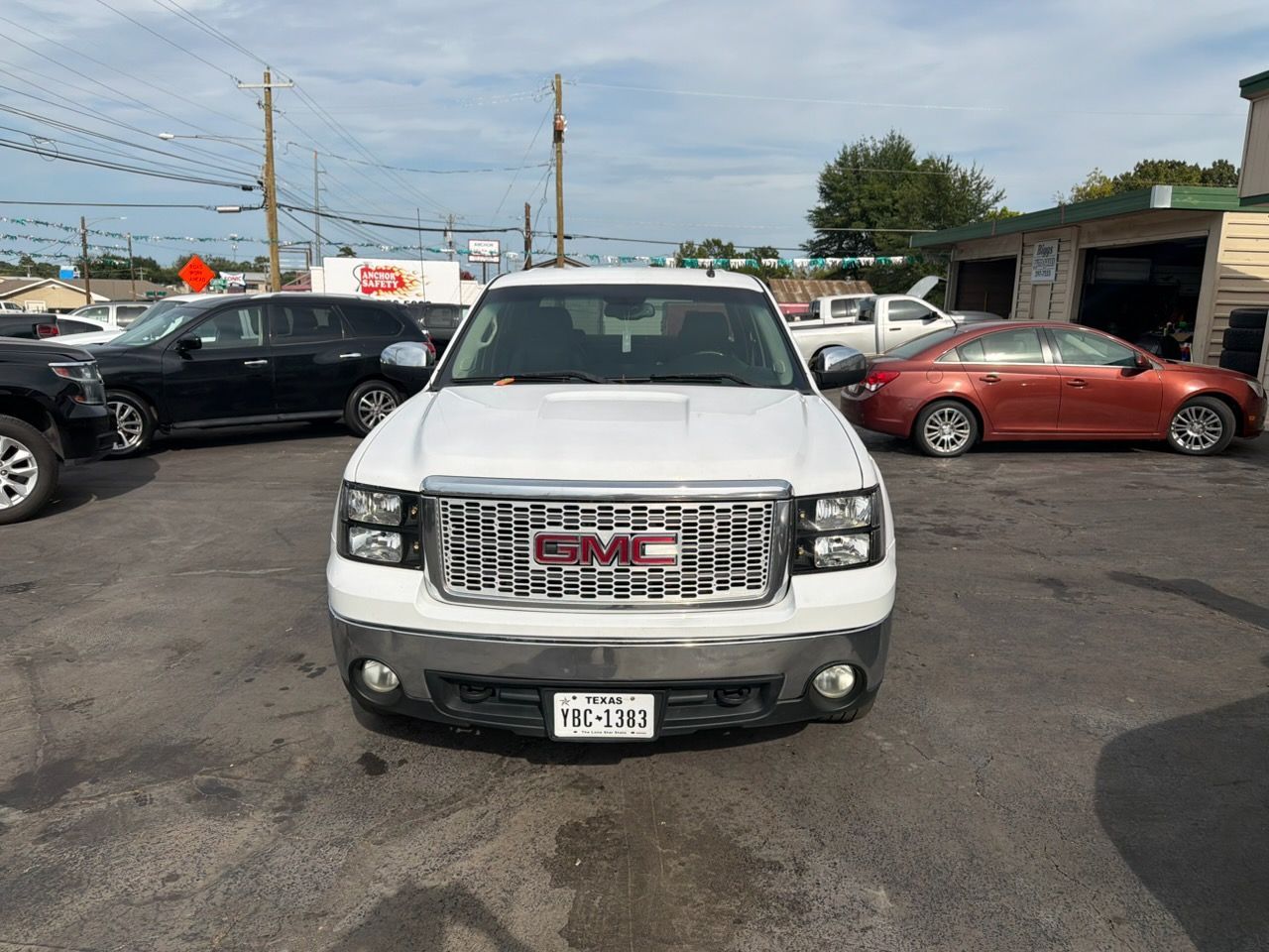 Front view of a white GMC SUV in a car lot, with a red car and other vehicles behind it.