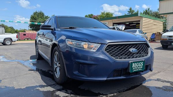 Blue Ford Taurus sedan parked in front of a car dealership on a sunny day.