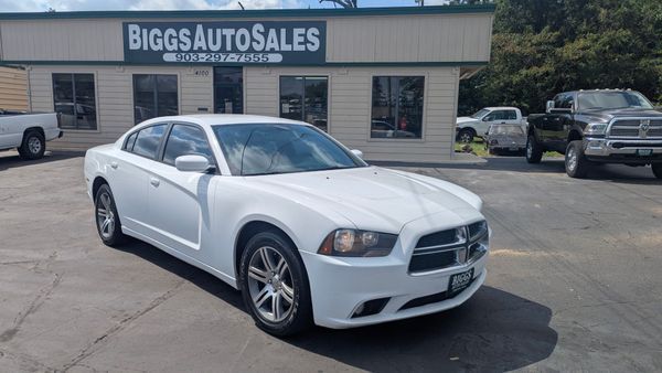 White Dodge Charger parked in front of Biggs Auto Sales, sunny day.