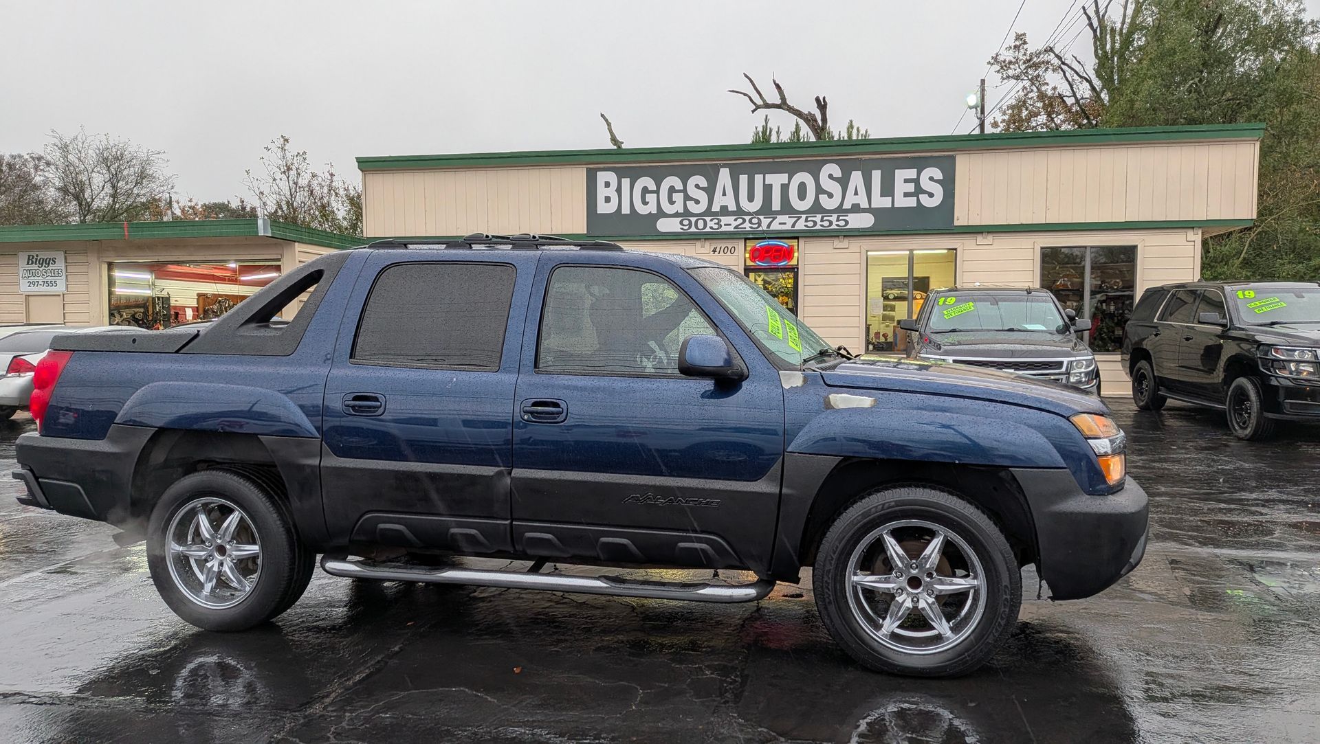 Blue Chevrolet Avalanche truck parked outside Bigos Auto Sales.