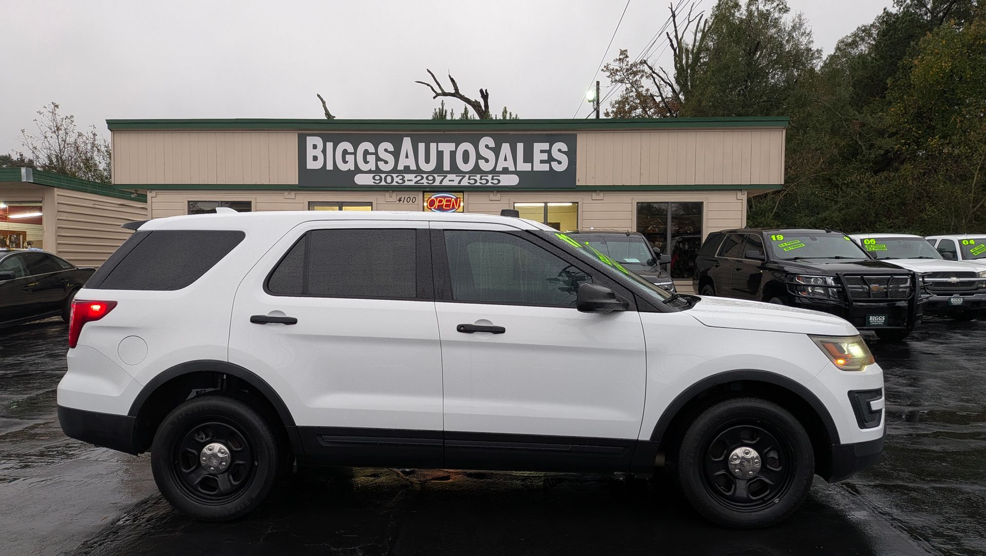 White police SUV parked in front of Biggs Auto Sales building on a rainy day.