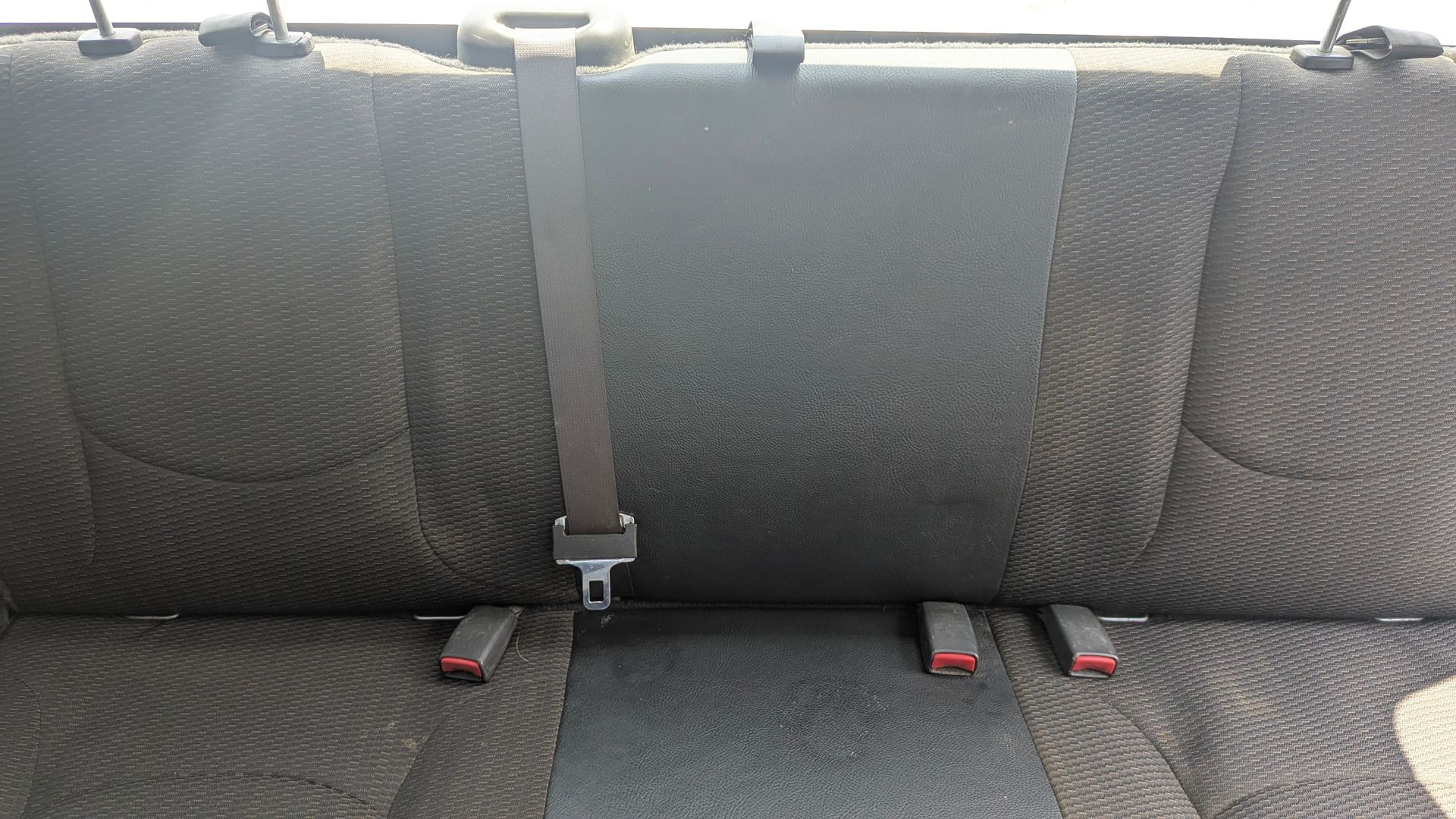 Car back seat with a middle seat belt and two lower buckles. Black textured fabric.