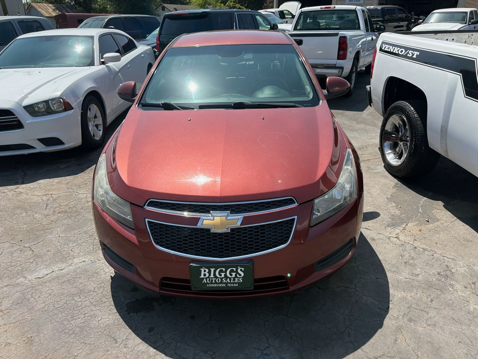 Red Chevrolet sedan parked in a lot, seen from the front between white vehicles.