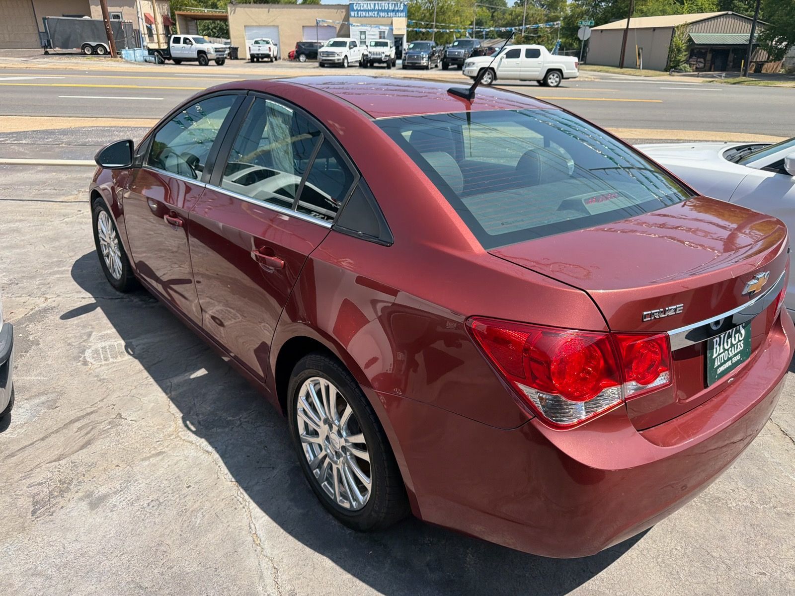 Red sedan parked in a sunny lot, rear three-quarter view.