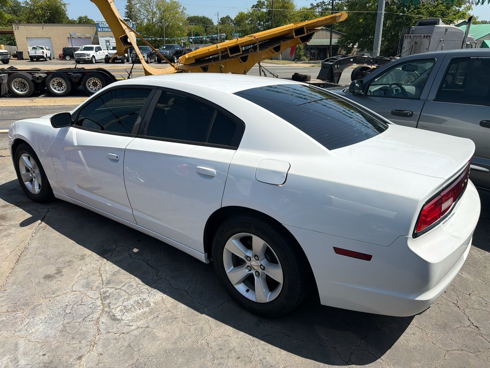 White sedan parked in a lot, viewed from the rear side on a sunny day.