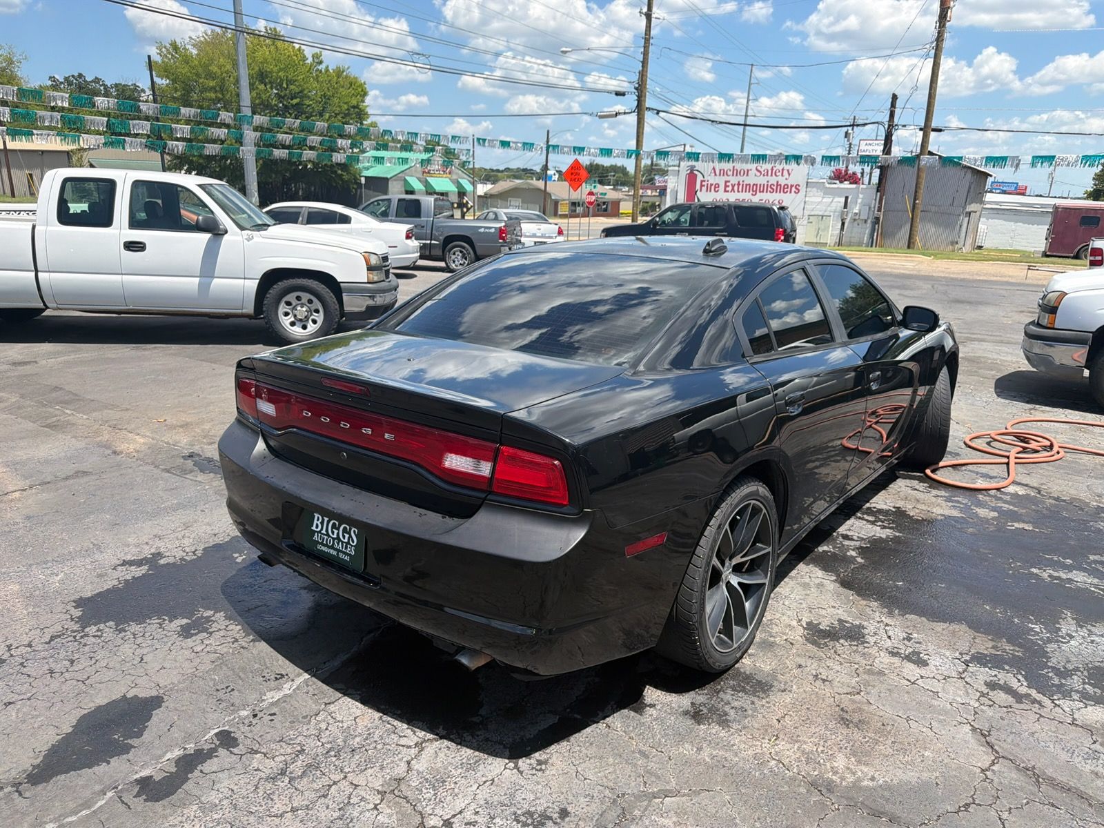 Black Dodge Charger parked in a lot with a white pickup nearby and road construction in the background