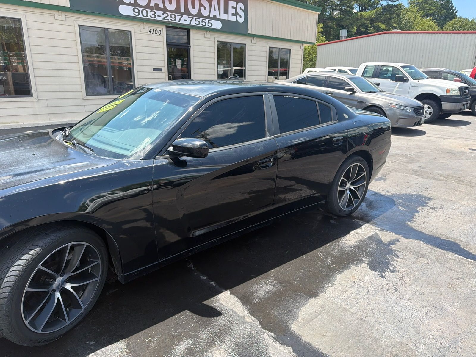 Black sports coupe parked in front of a used car dealership building