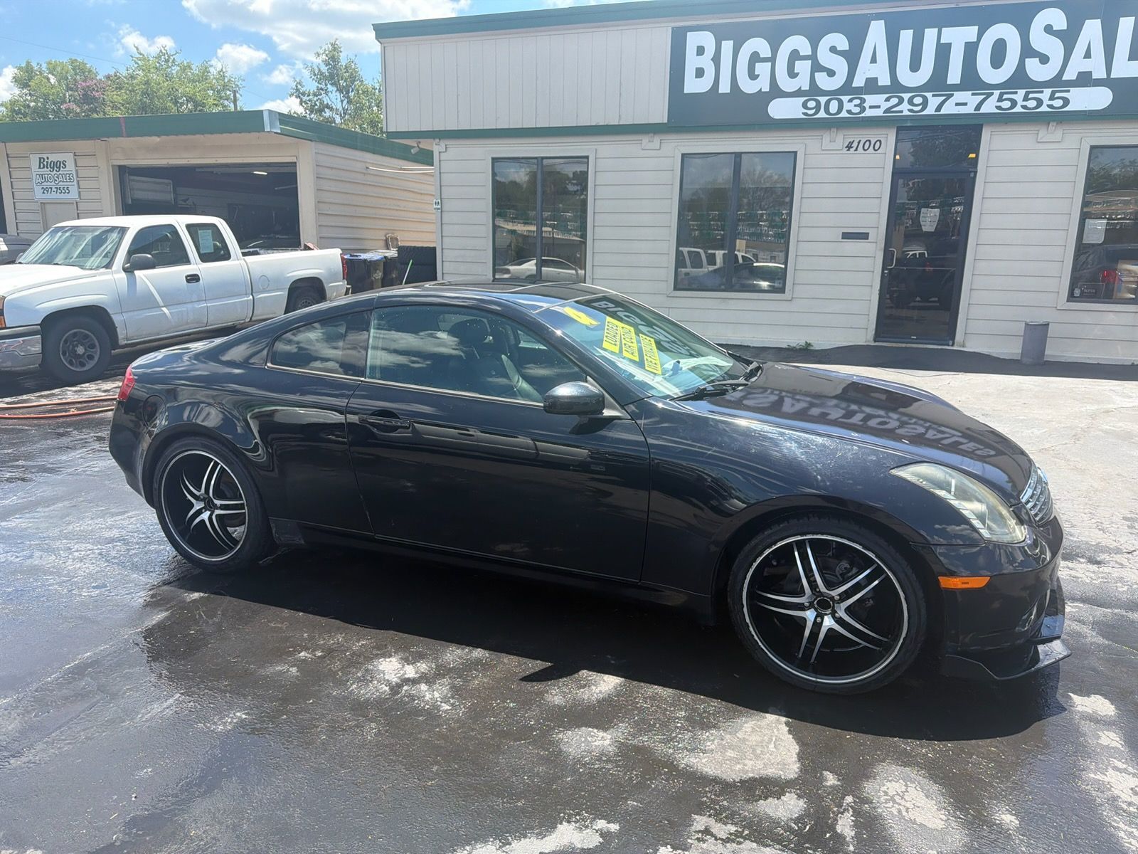 Black sedan parked outside Biggs Auto Sales on a wet lot.