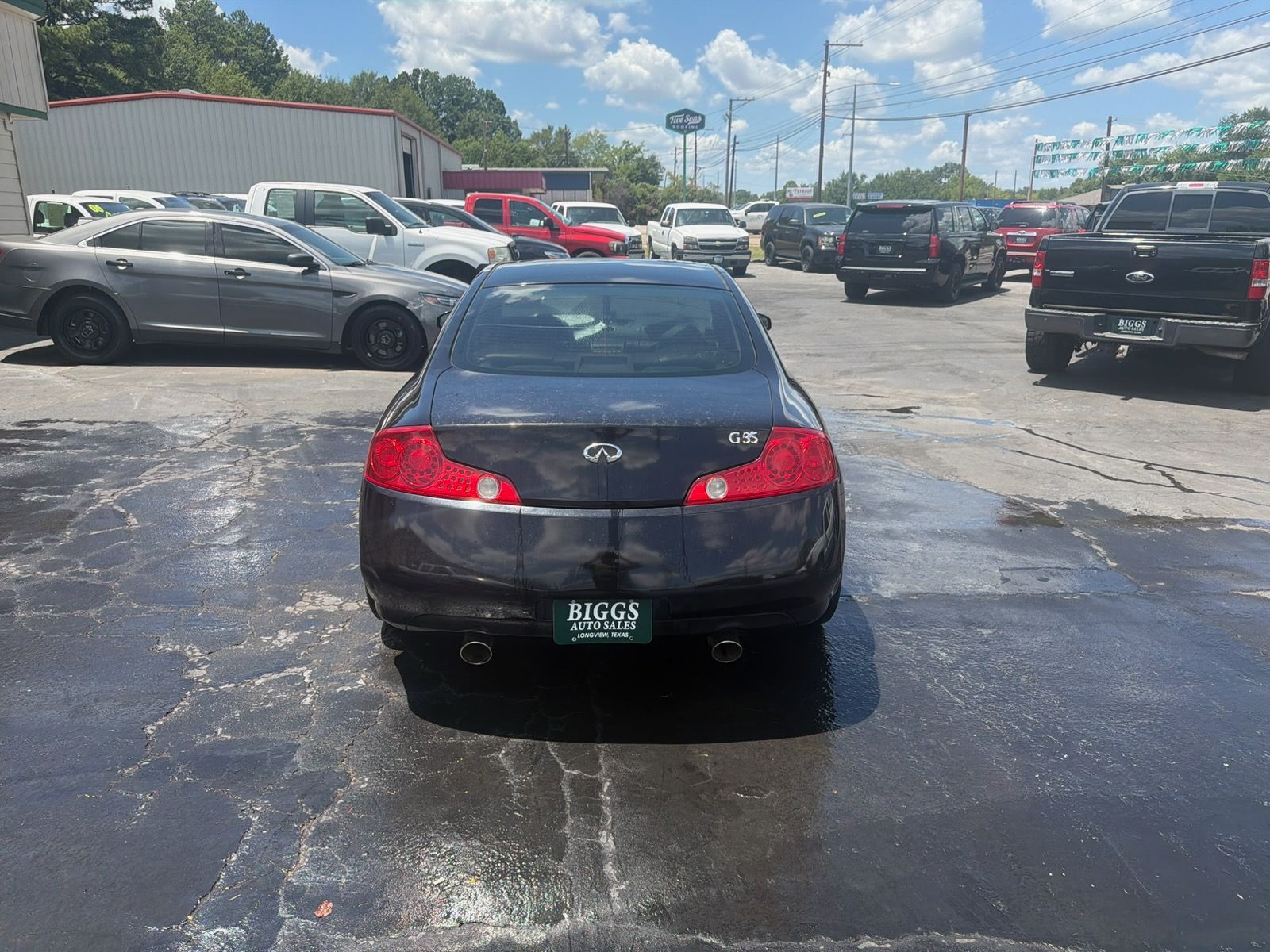 Black car parked in a dealership lot with other vehicles under a sunny sky.