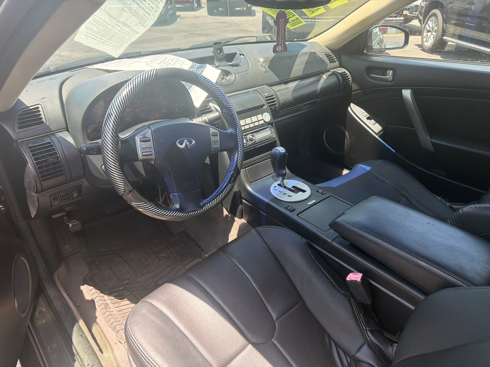 Car interior with black leather seats, blue steering wheel cover, and center console in sunlight