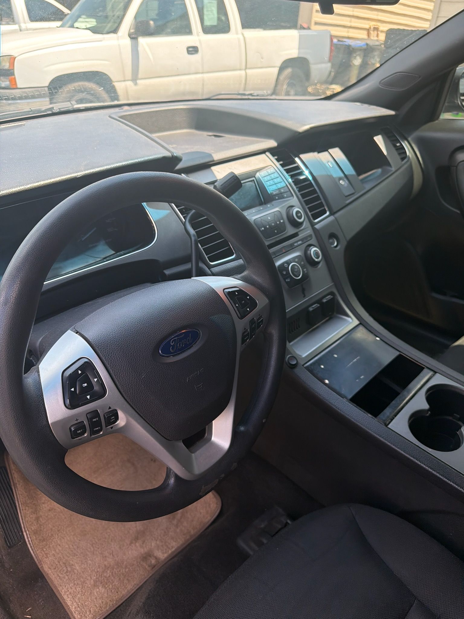 Car interior with steering wheel, dashboard, center console, and front seats, viewed from the driver’s side.
