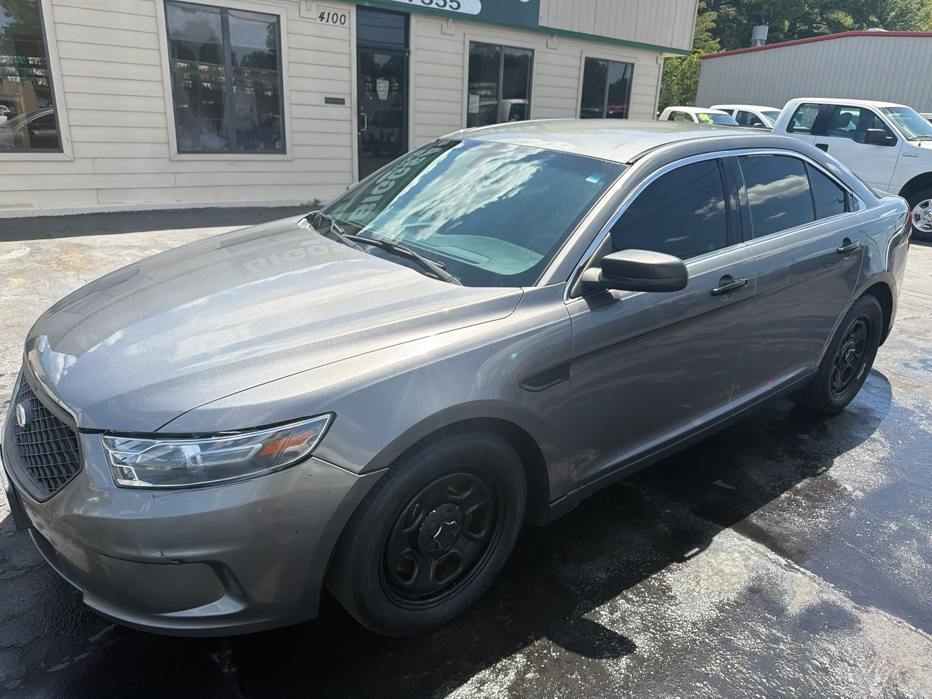 Gray sedan parked outside a building on a wet lot, with dark-tinted windows and black wheels