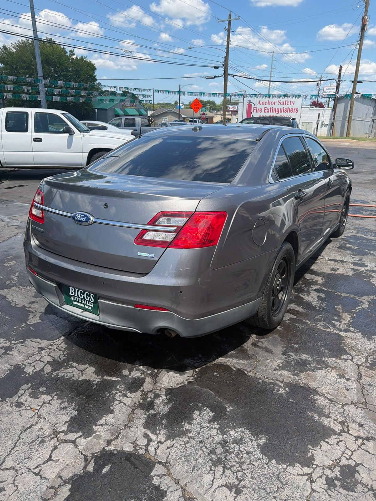 Gray sedan parked on cracked asphalt lot near a white pickup truck and chain-link fence
