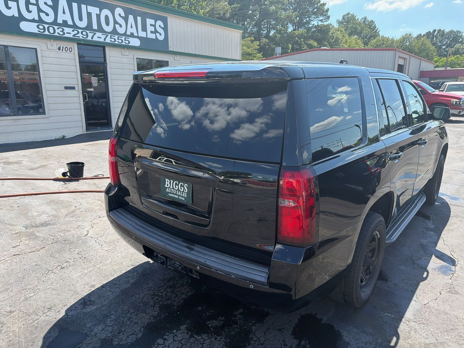 Black SUV parked at an auto sales lot in bright daylight, rear three-quarter view.
