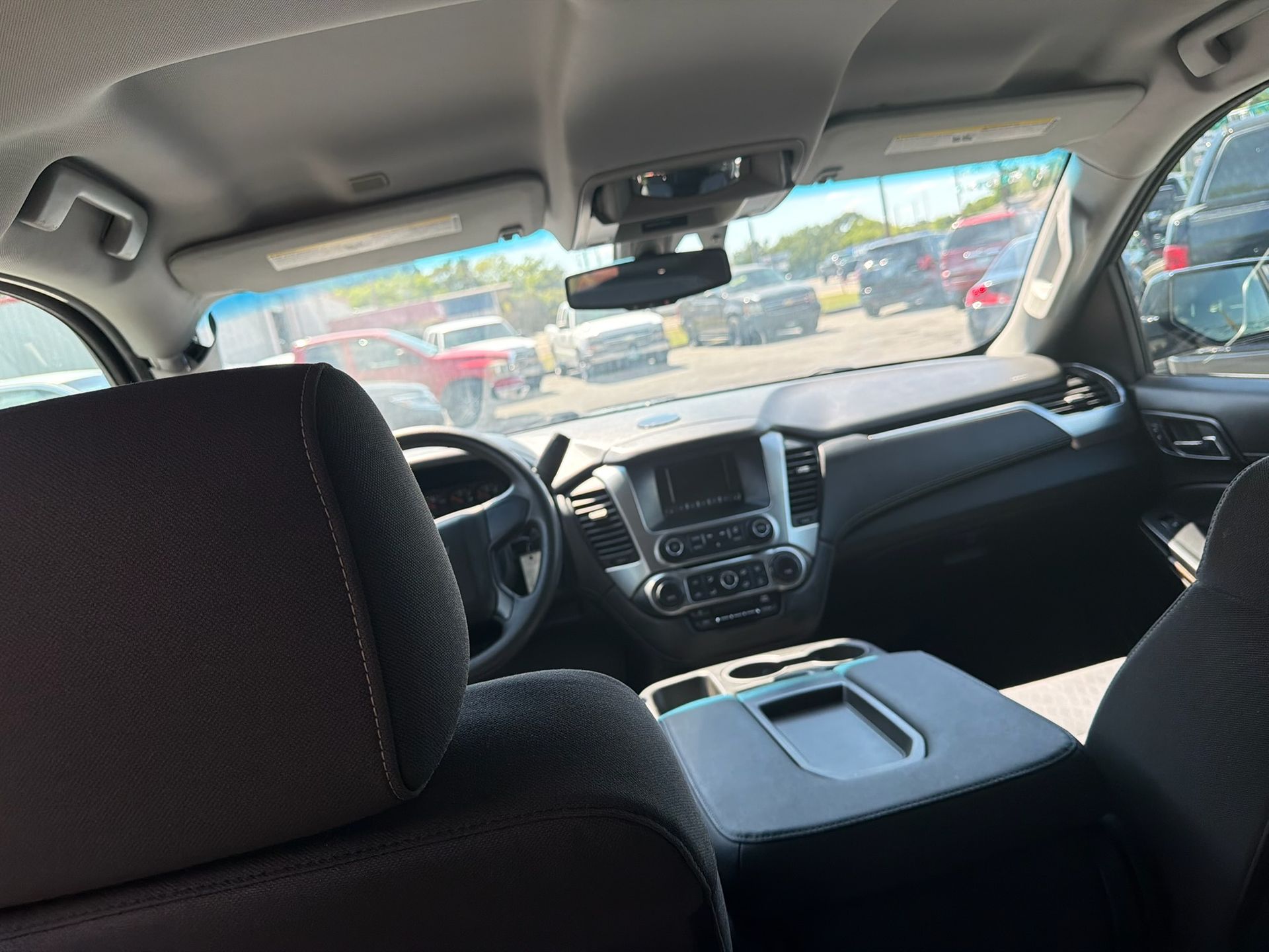 Inside a car looking forward from the back seat at the dashboard, steering wheel, and windshield view of parked cars.