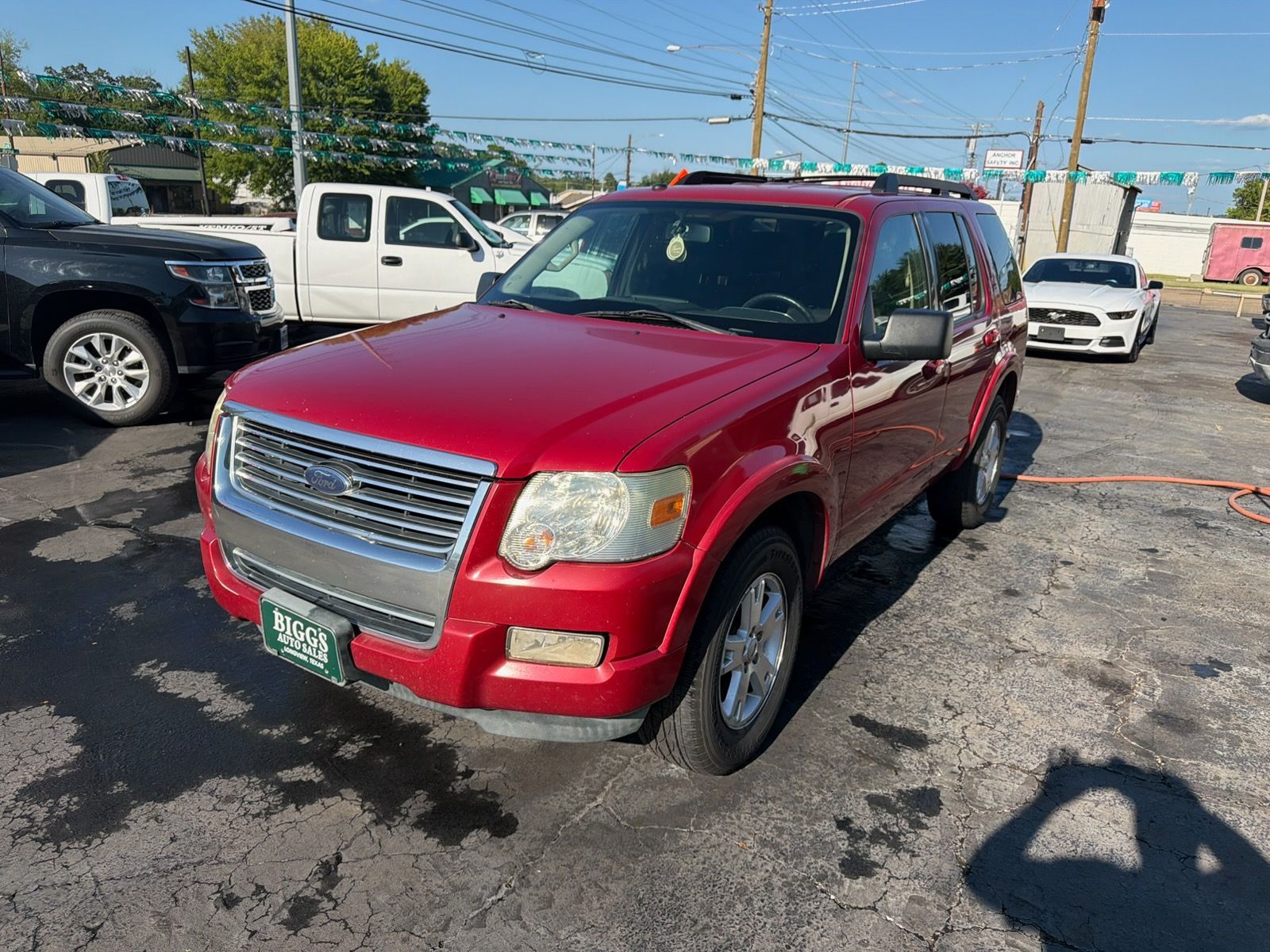 Red SUV parked on a lot under a sunny sky, with other cars in the background.
