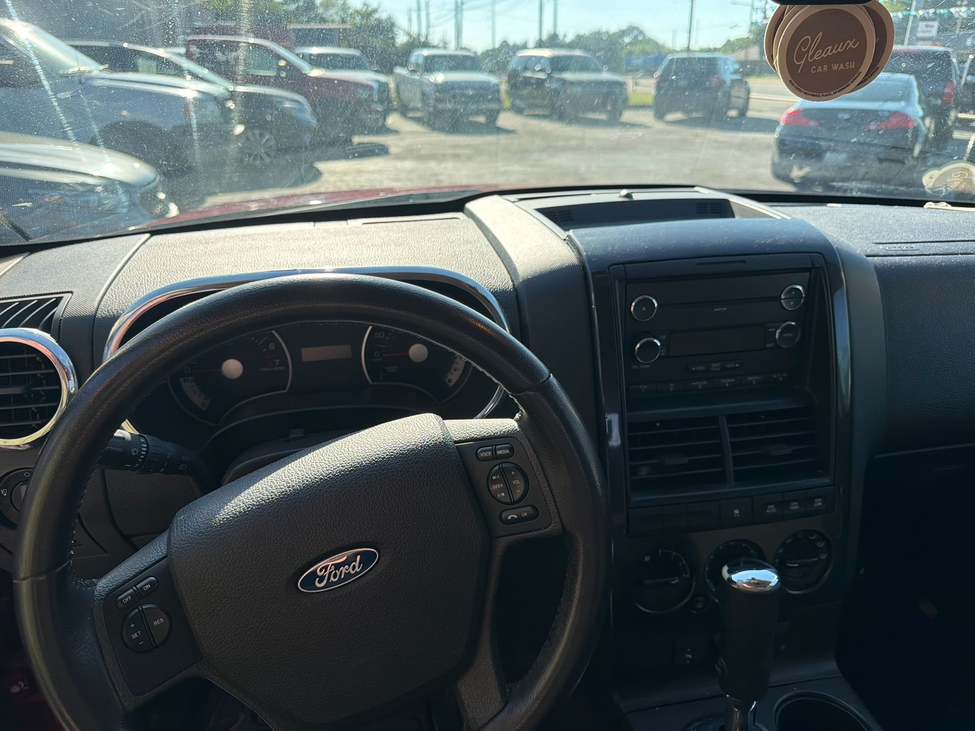 View from driver’s seat of a Ford car interior parked in a lot, with dashboard, steering wheel, and hanging ornament visible.