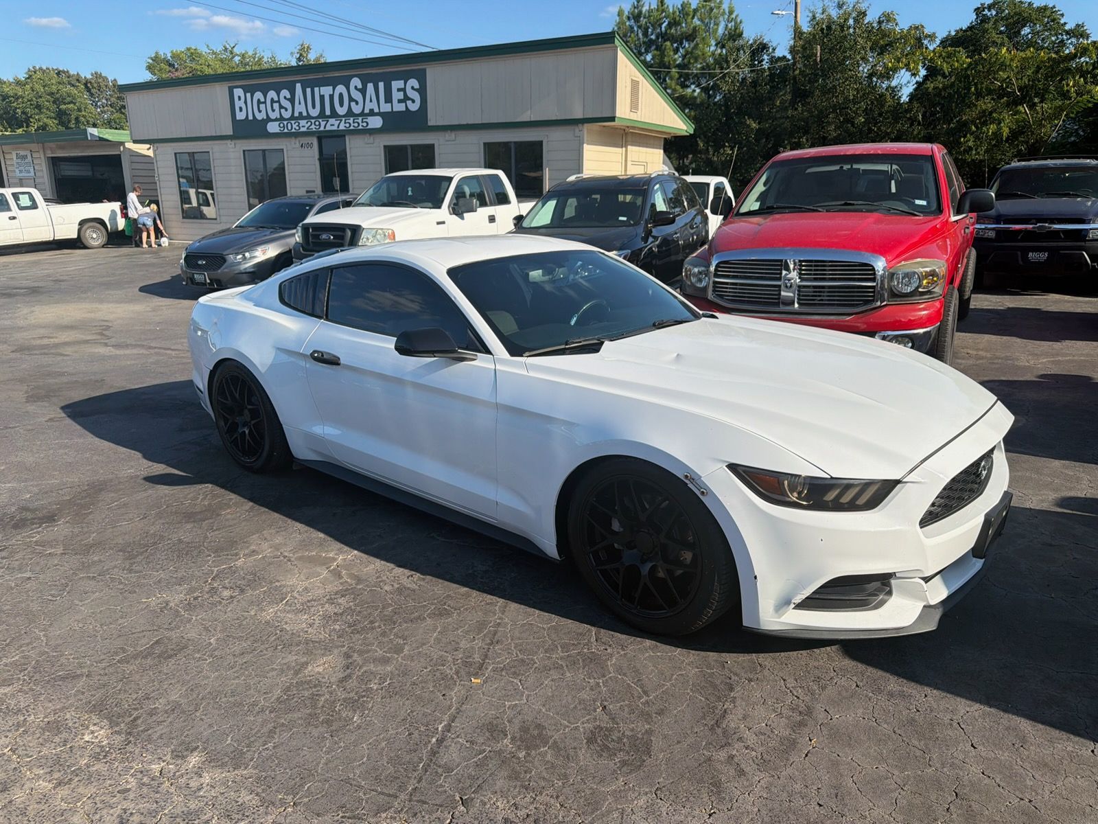 White sports coupe parked outside an auto sales lot with a red truck behind it