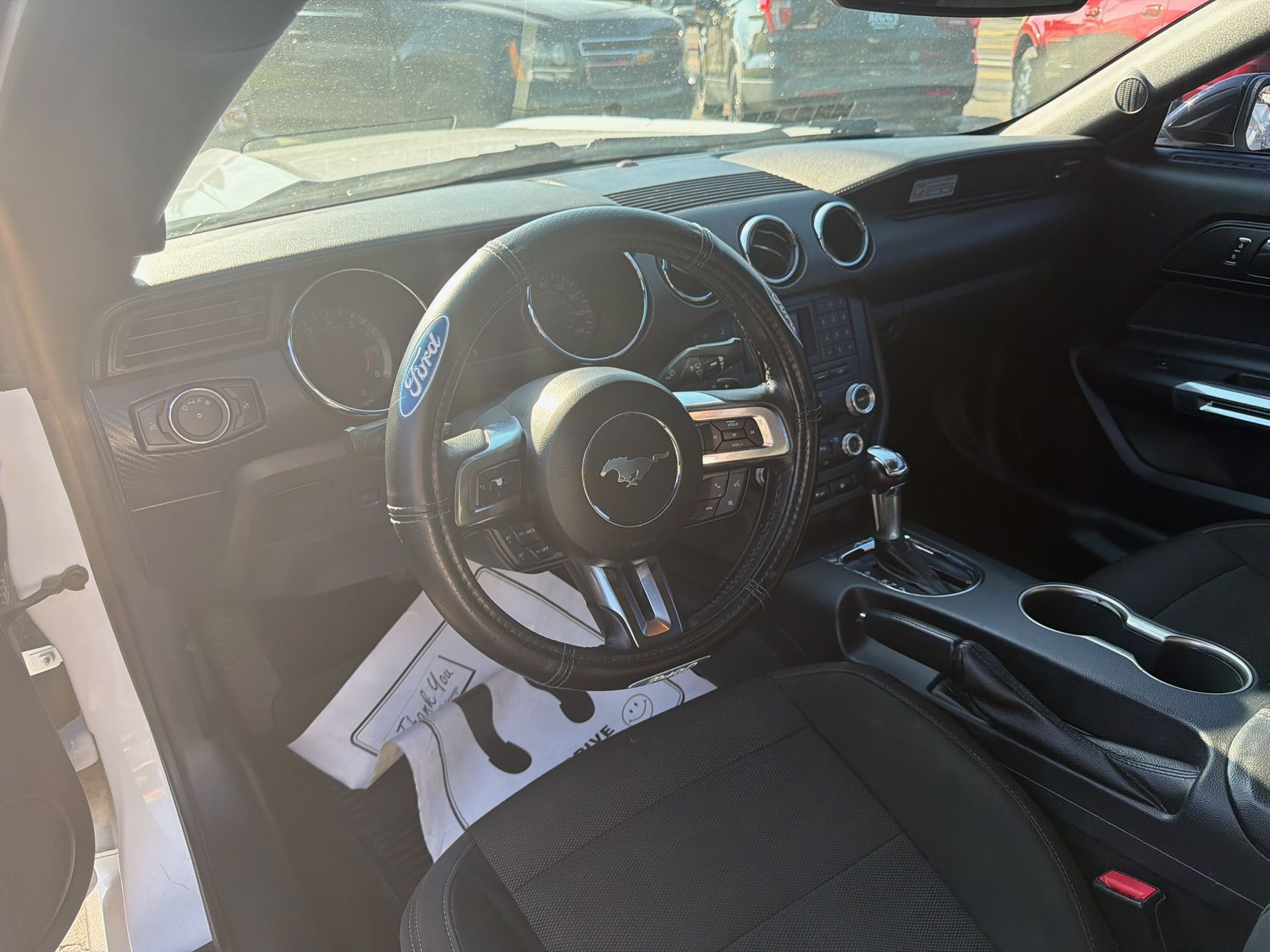 Car interior with a custom black steering wheel, dashboard gauges, and cup holders visible.