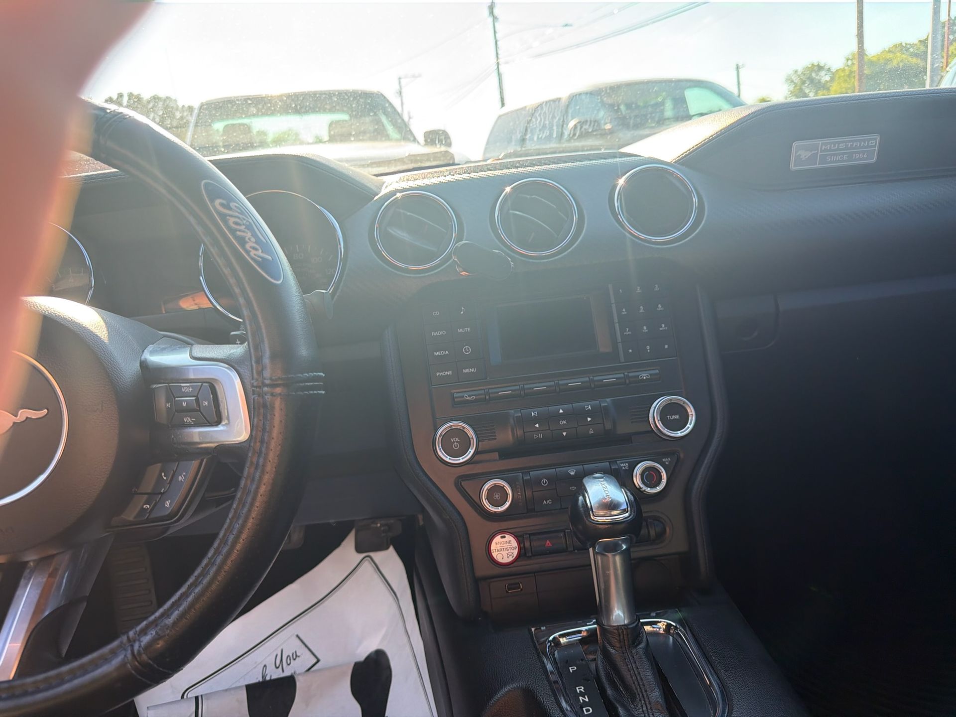 Car dashboard interior with steering wheel, center console, and bright sunlight through the windshield